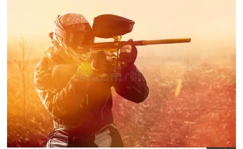 Paintball player firing marker at sunset in open outdoor field