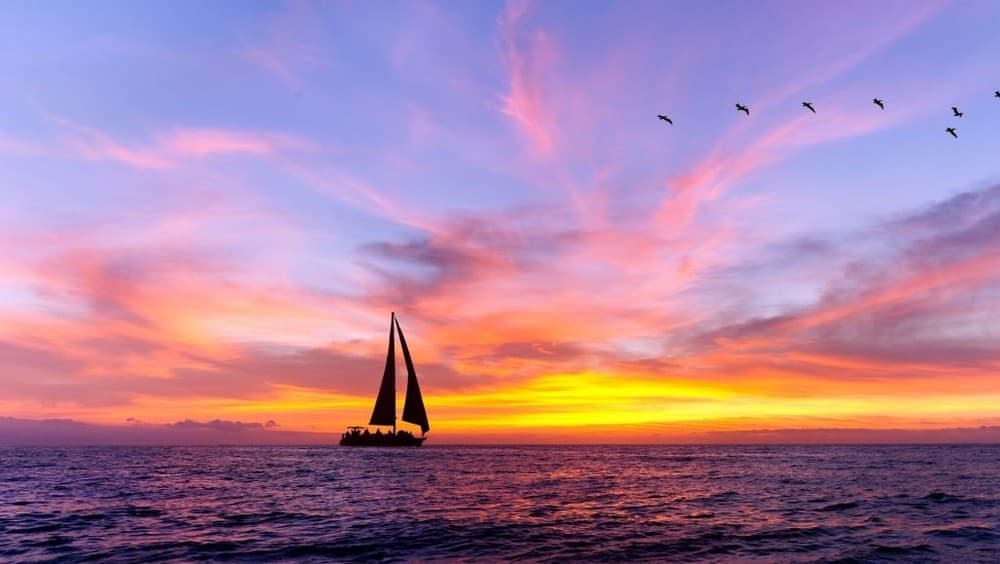 Solo sailboat silhouetted against vivid tropical sunset horizon