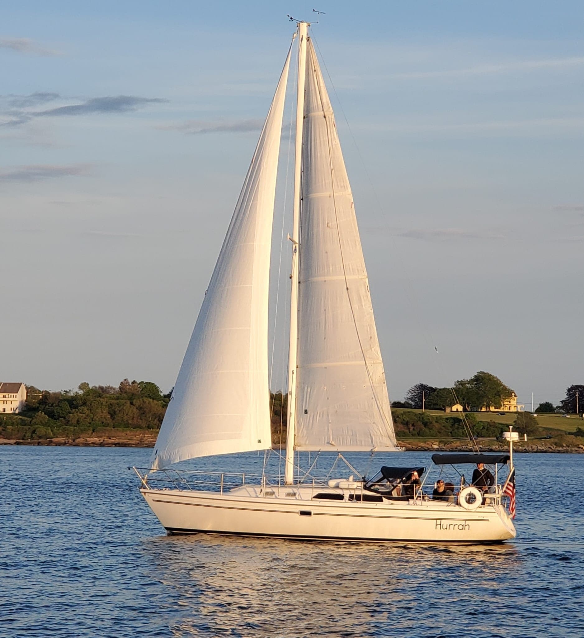 White sailboat sailing offshore near coastal shore at golden hour