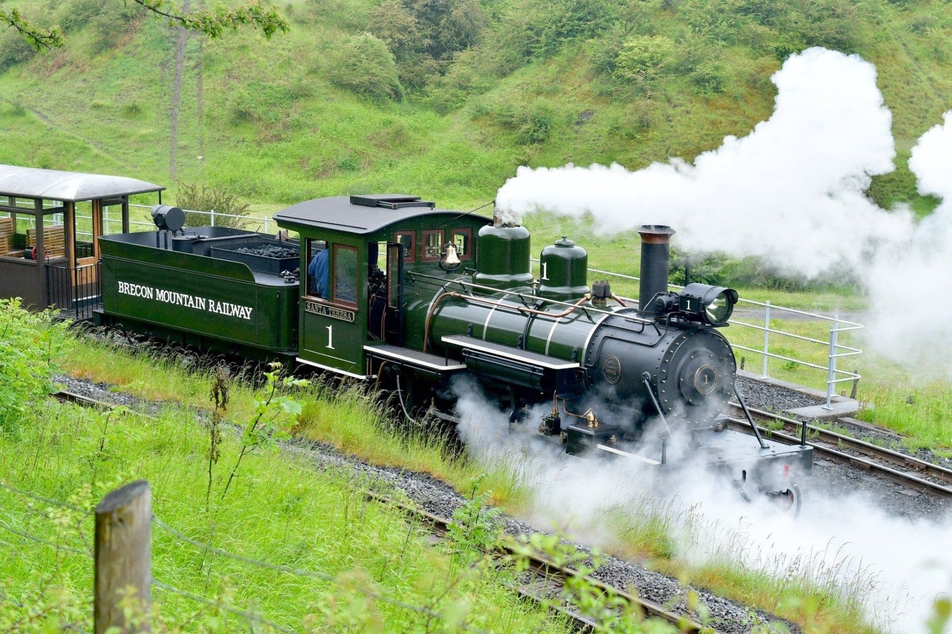 Steam train traversing green hills emitting white smoke