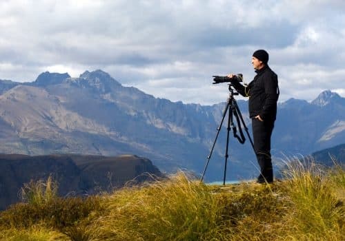 Photographer with tripod on alpine ridge overlooking mountain range