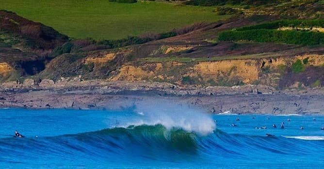 Large blue wave breaking by cliff at Croyde Bay, surfing scene