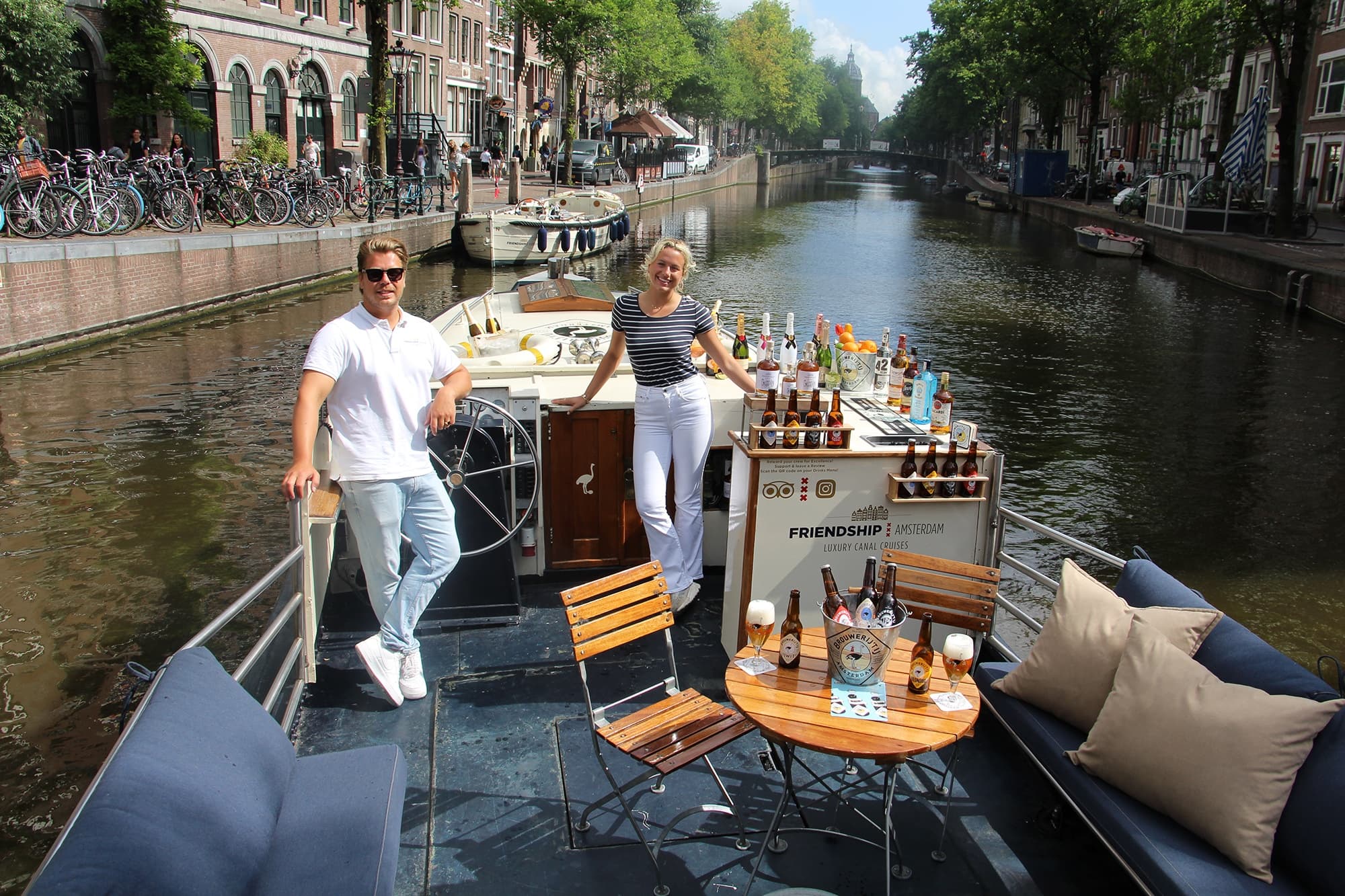 Friends on Amsterdam canal boat deck posing with cocktails