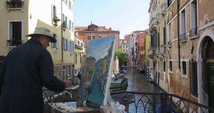 Artist painting Venice canal scene on an outdoor bridge