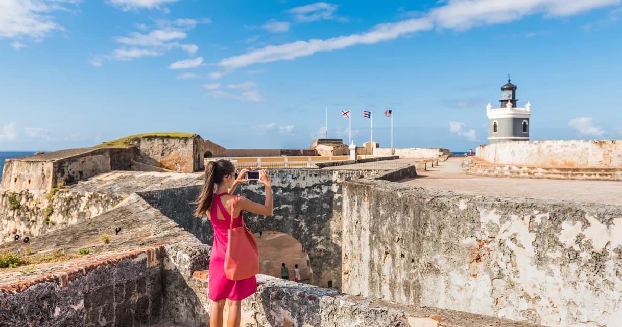 Traveler photographing coastal fort and lighthouse on sunny shore