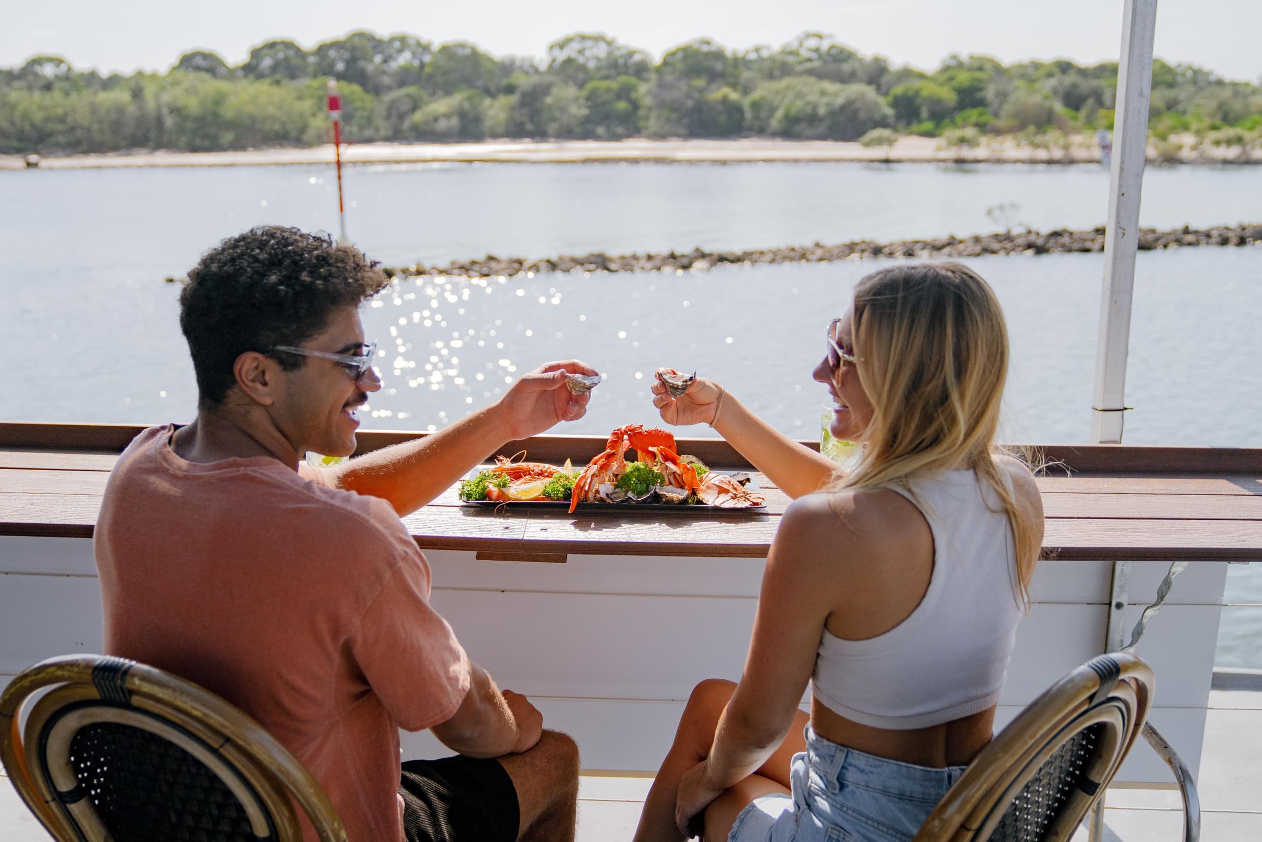 Couple dining on cruise deck with waterfront views and casual drinks