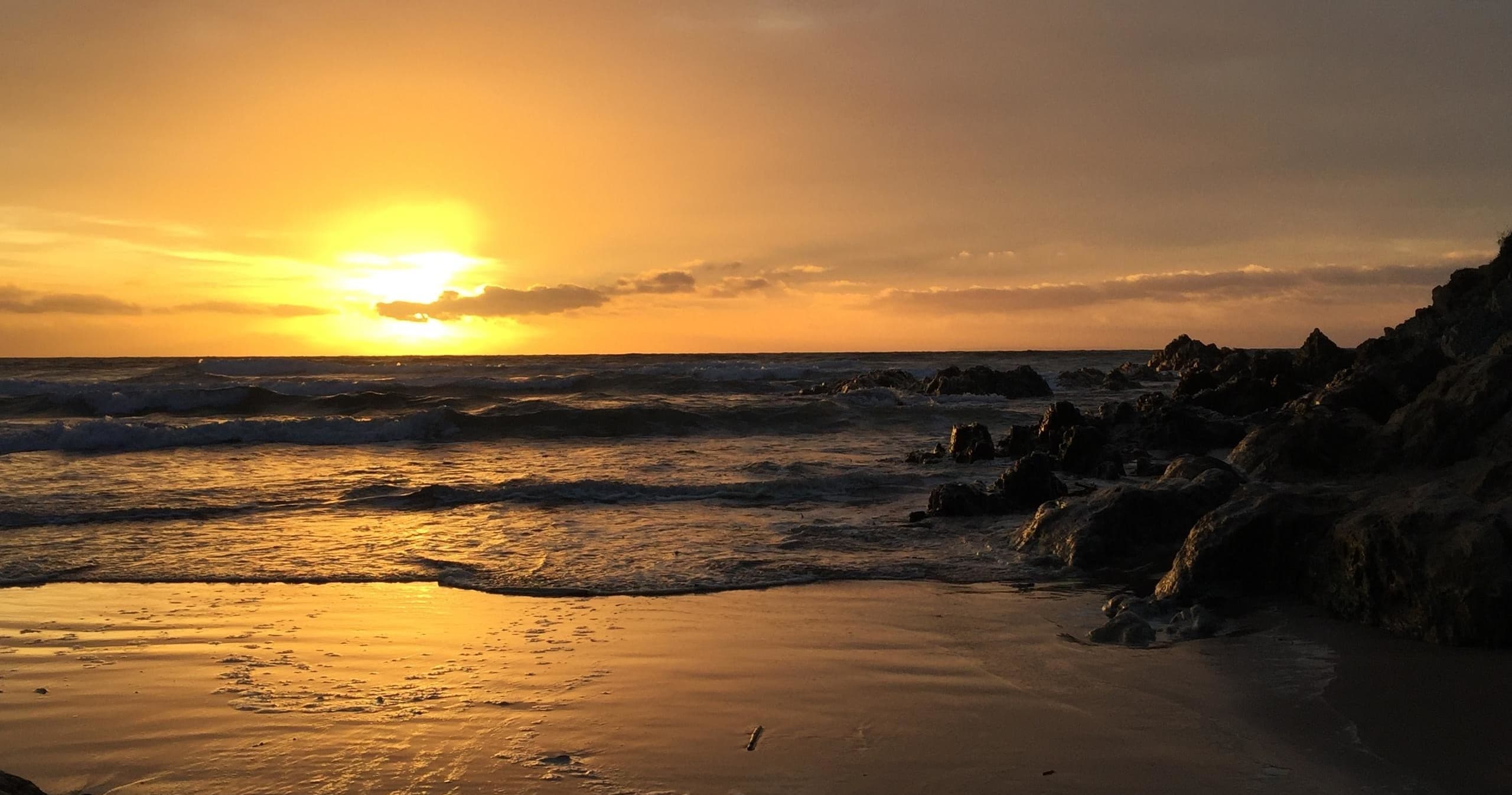 Sunset over ocean beach and rocky shoreline at dusk