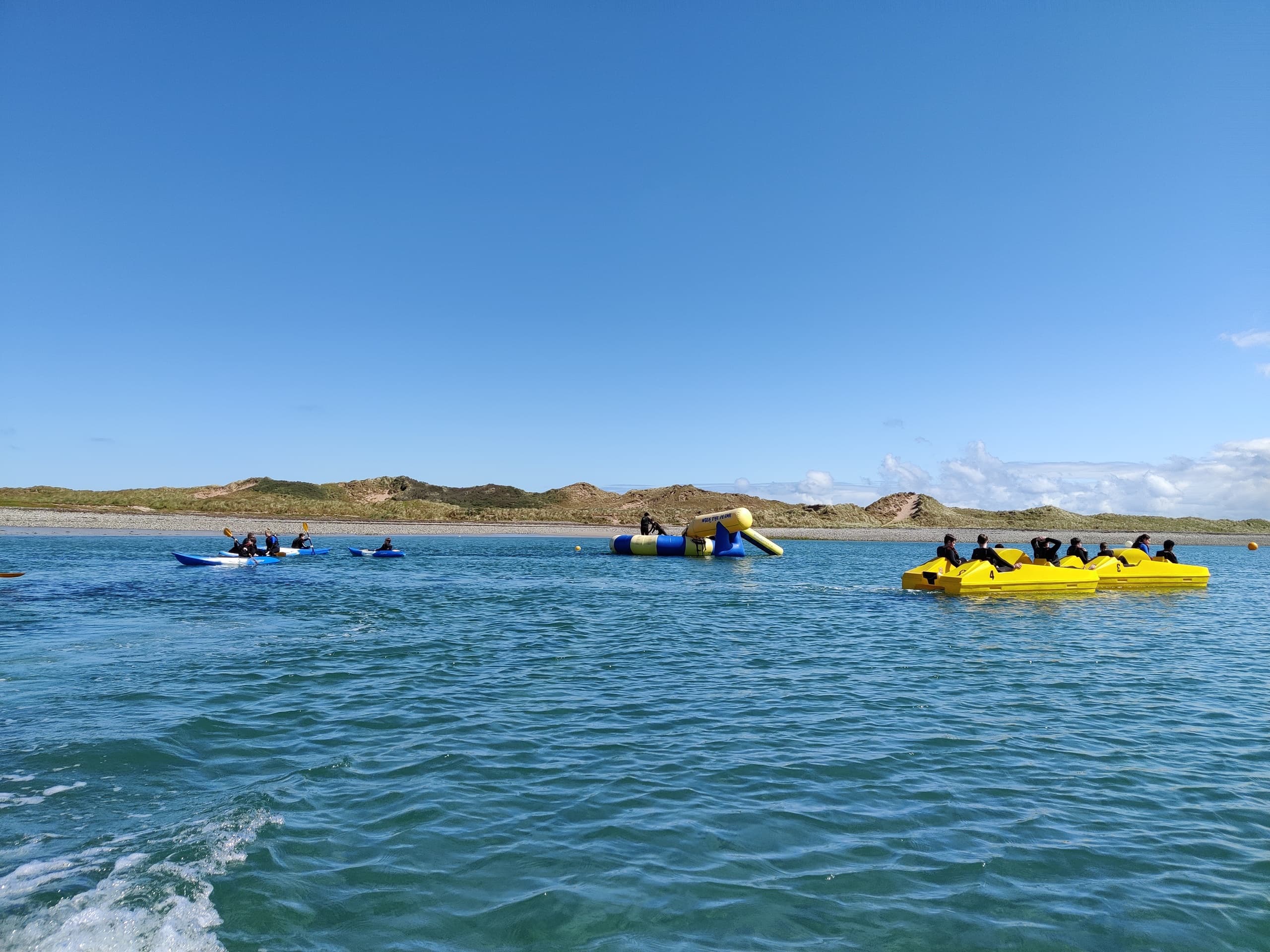 Kayakers paddling on open coastal waters with dunes backdrop