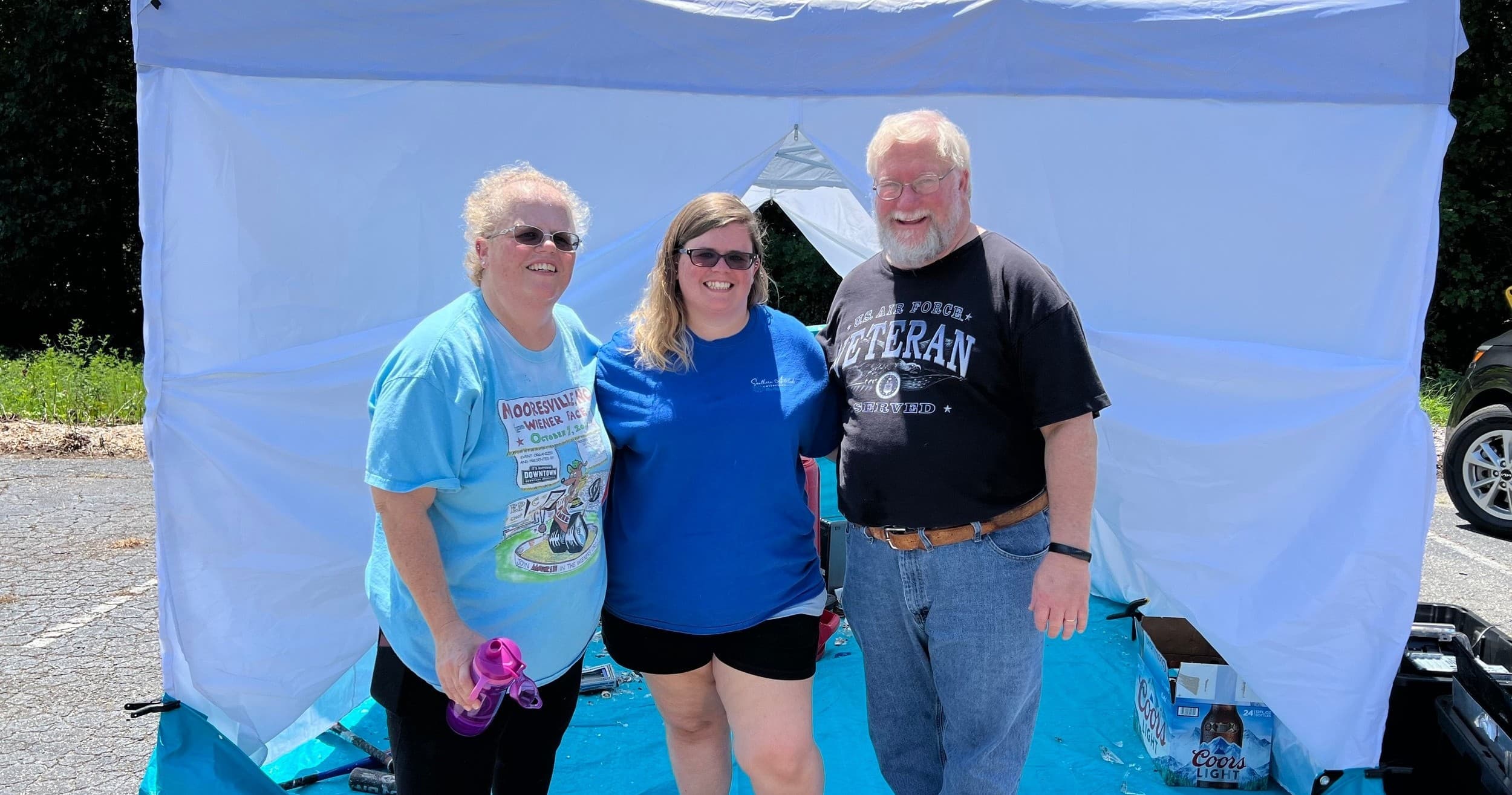 Three staff posing at Warrior Rage Room outdoor pop-up tent