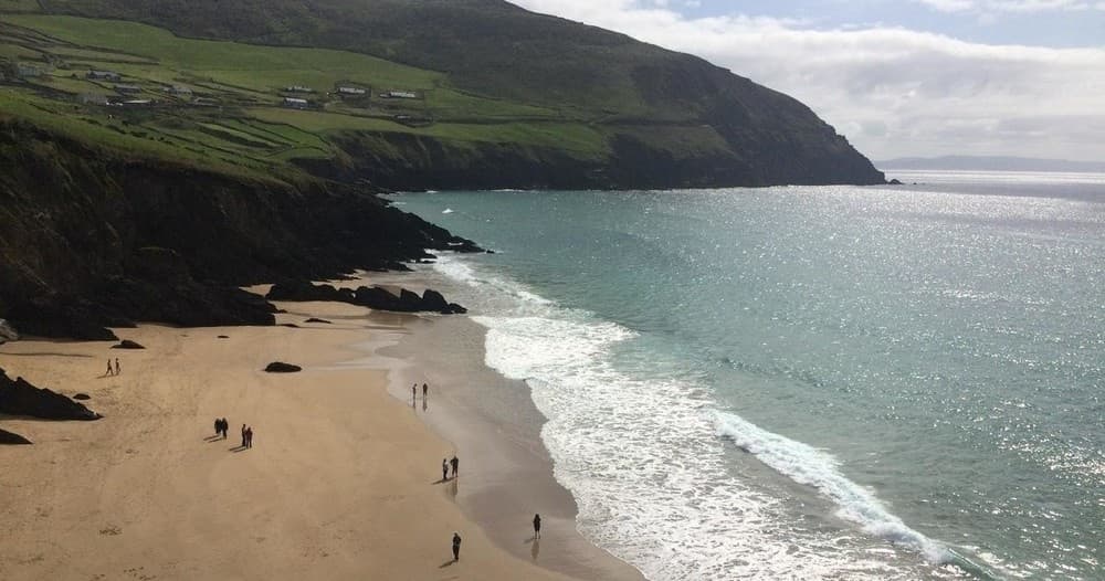 Sandy bay and surf with beachgoers, coastal walk and sea views