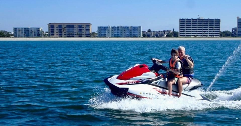 Two riders on red jet ski speeding past seaside condos