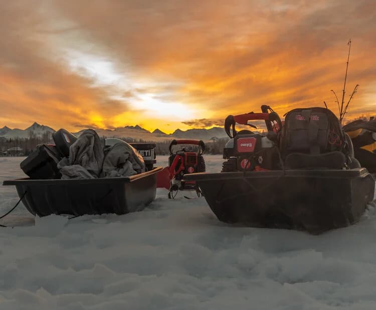 Skiffs and fishing gear on snowy shore at sunrise with mountains