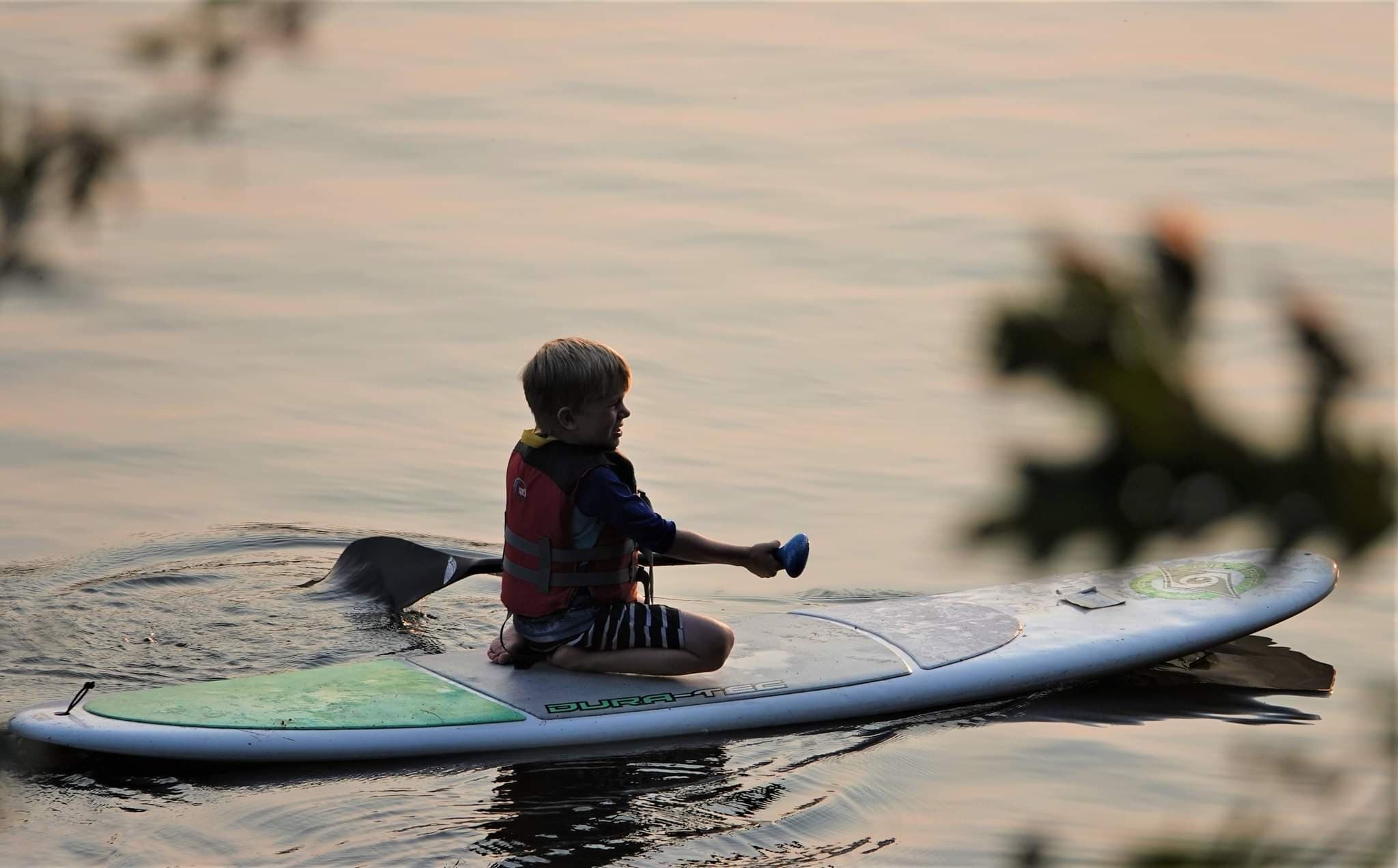 Child sitting on paddleboard at sunset on tranquil lake