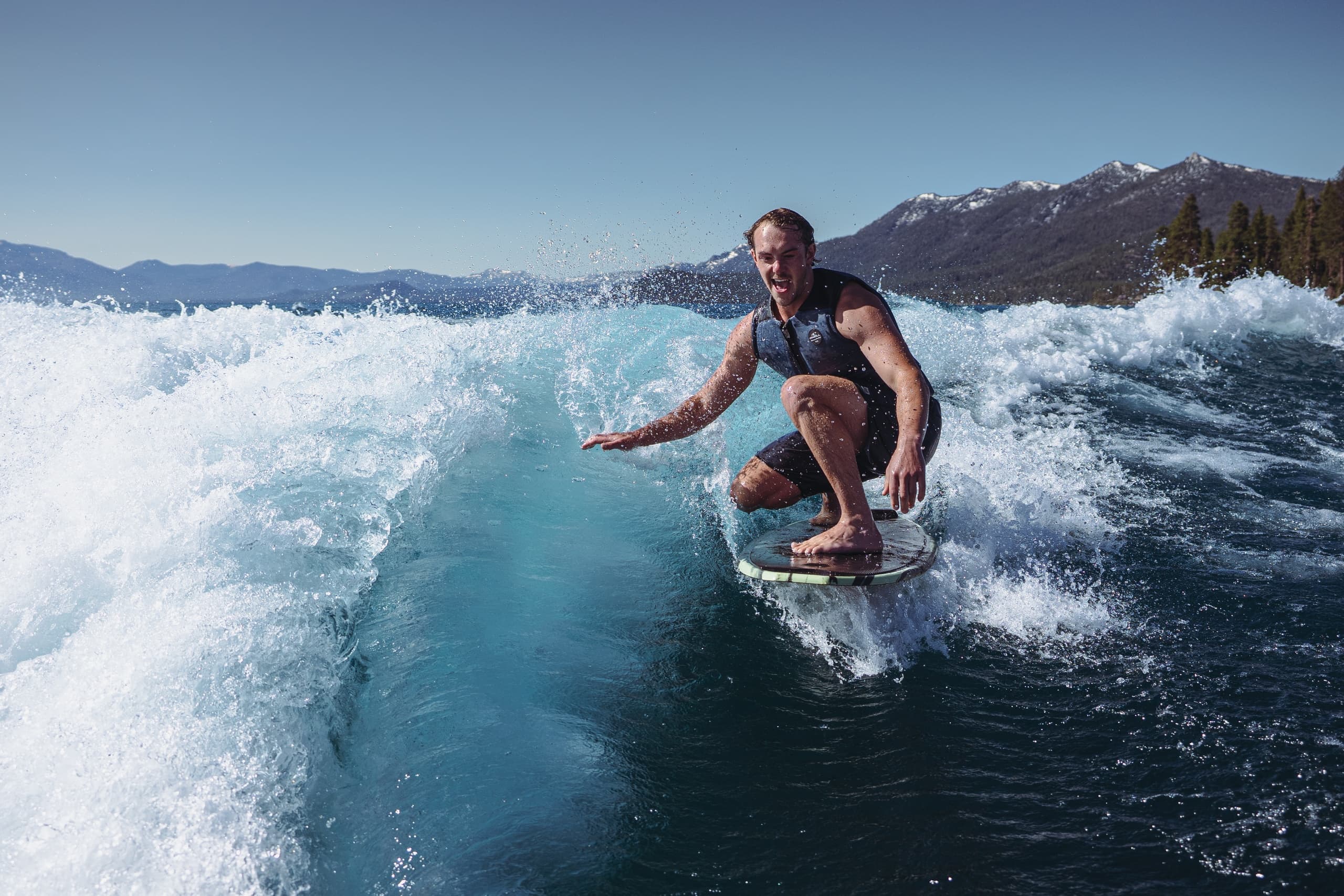 Wakesurfer riding a lake wake with mountain shoreline backdrop