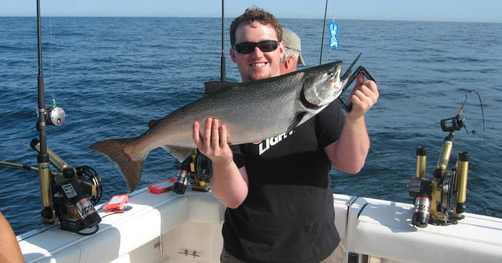 Angler holding large salmon on boat deck during offshore trip