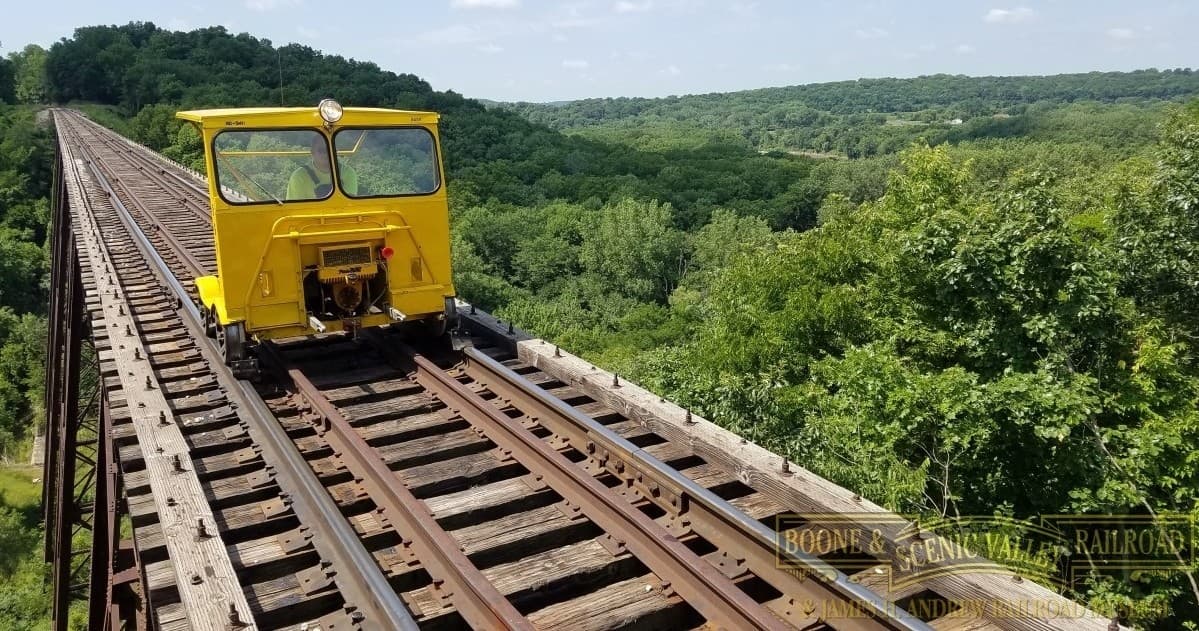 Rail maintenance trolley on wooden trestle above green forest
