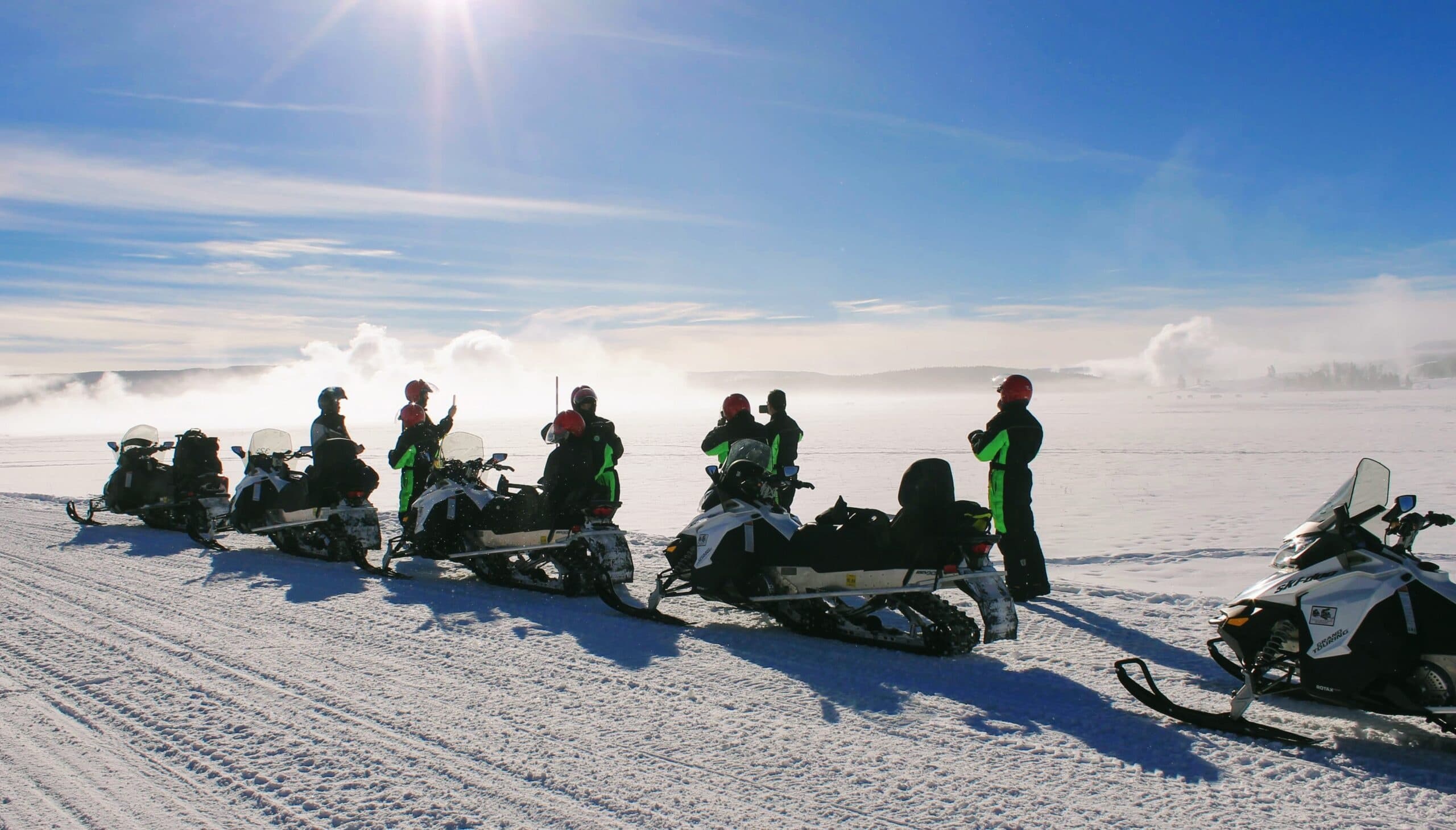 Snowmobilers lined up on snowy plain at sunrise in Yellowstone