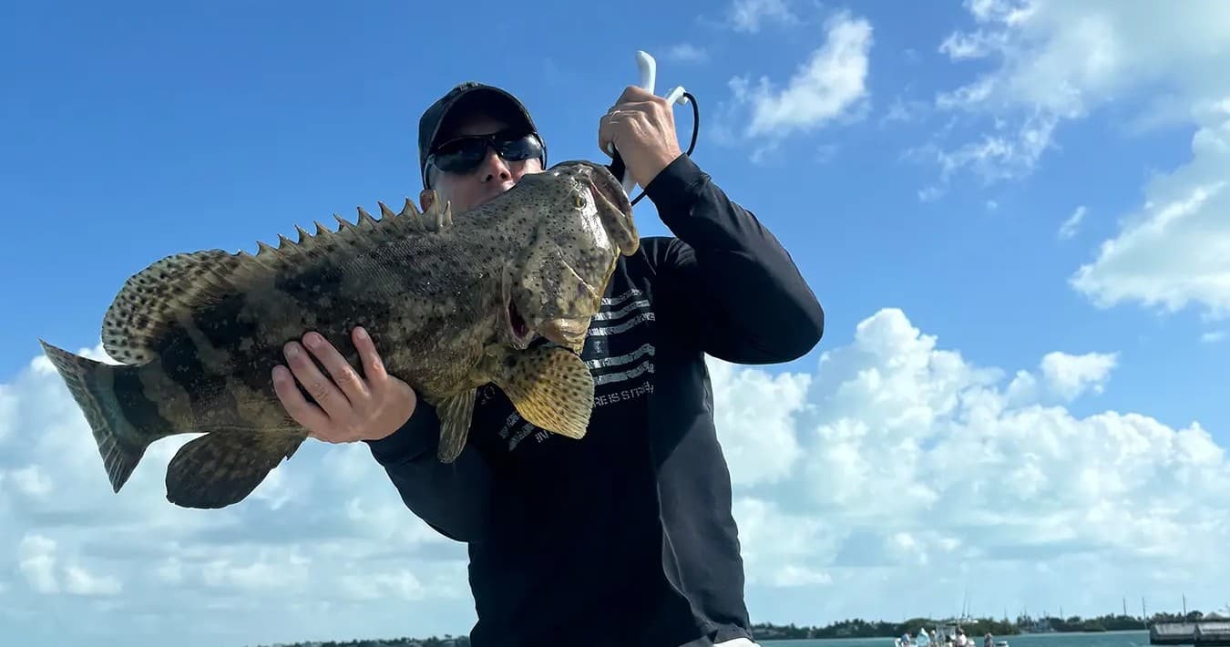 Angler holding large grouper on boat with blue sky backdrop
