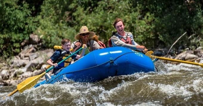 Close-up of rafters paddling turbulent river amid forested banks