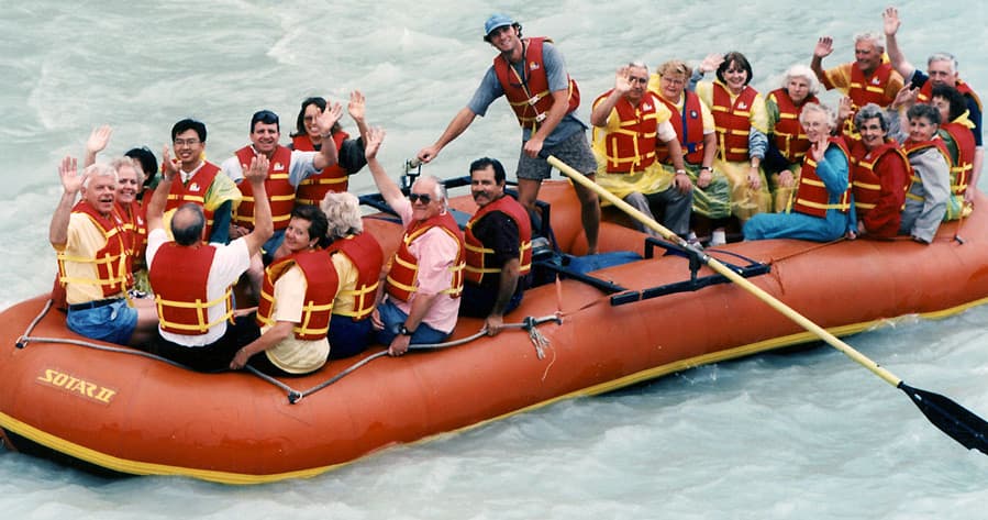 Large group whitewater rafting on churning river wearing lifejackets