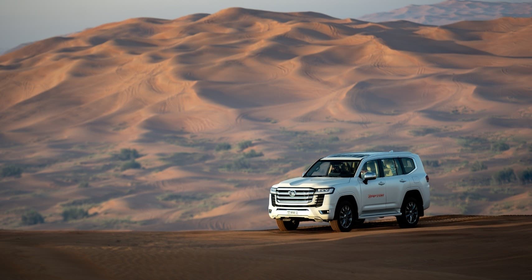 White SUV driving across rolling desert dunes on safari tour