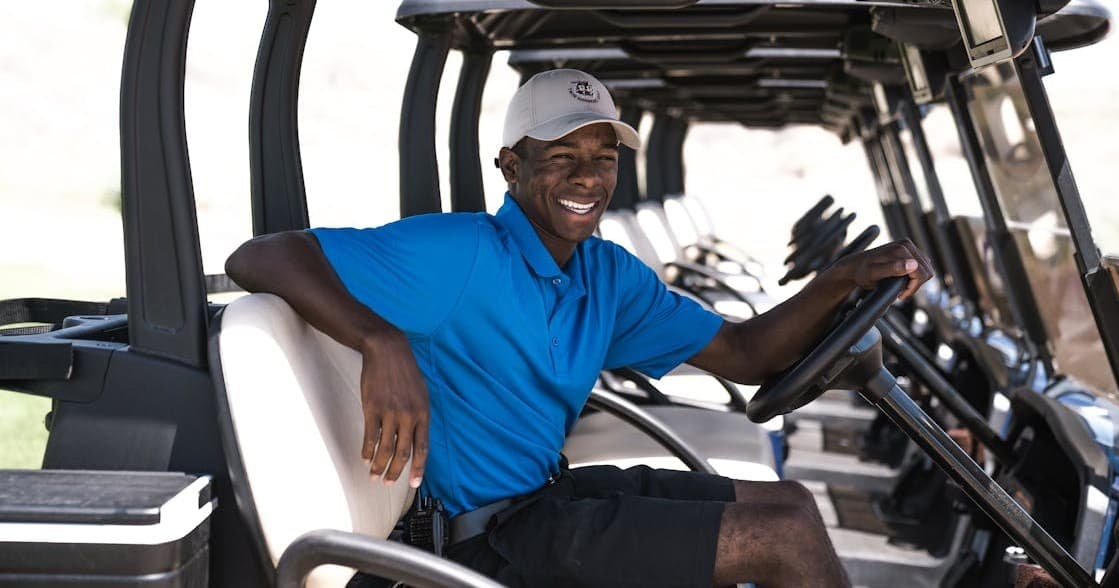 Smiling golf cart attendant seated in row of carts at course