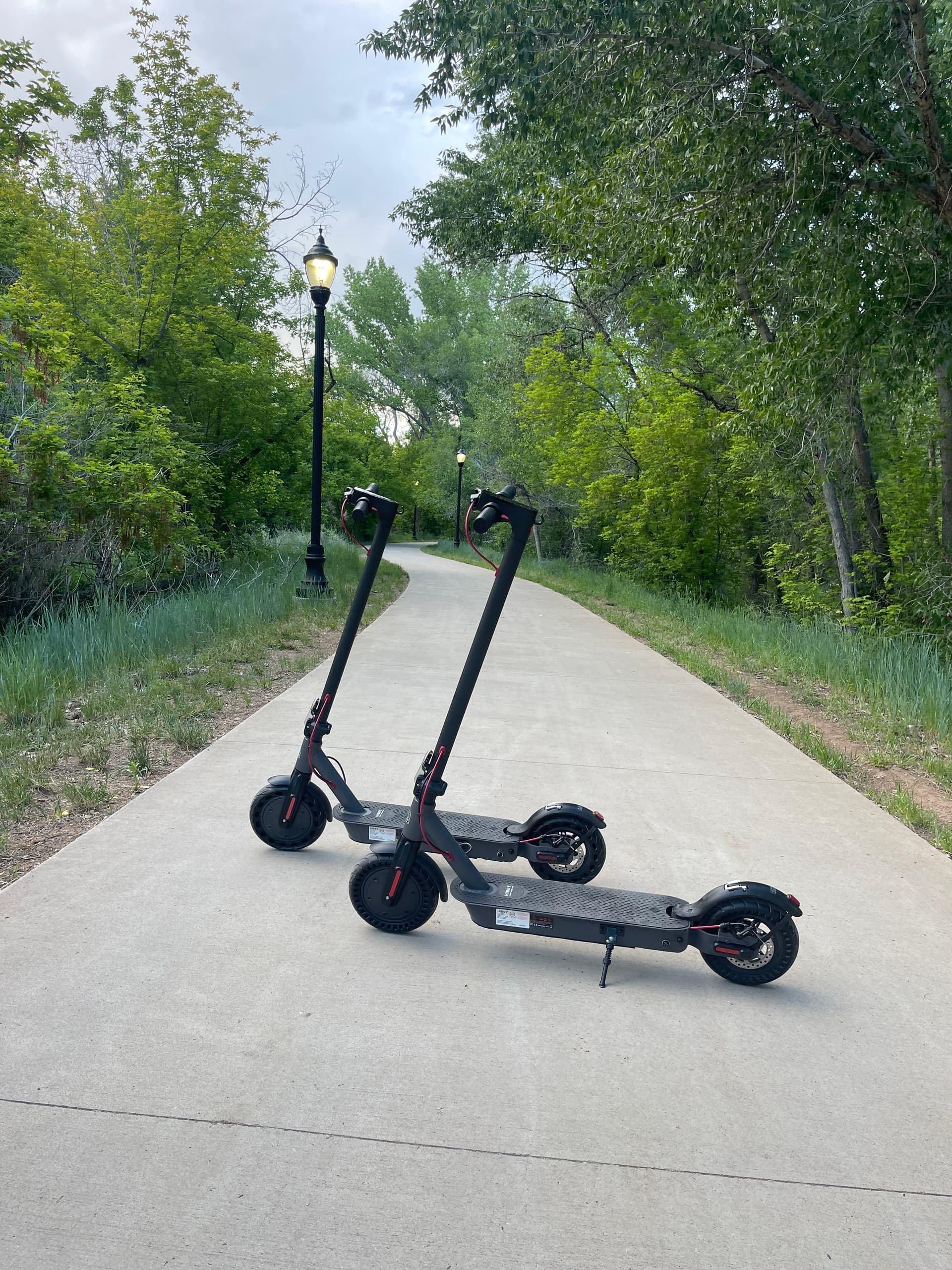 Three e-scooters on paved trail through green parkway