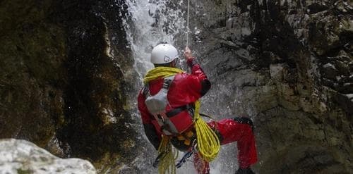 Canyoning guide rappelling down rocky waterfall in narrow gorge