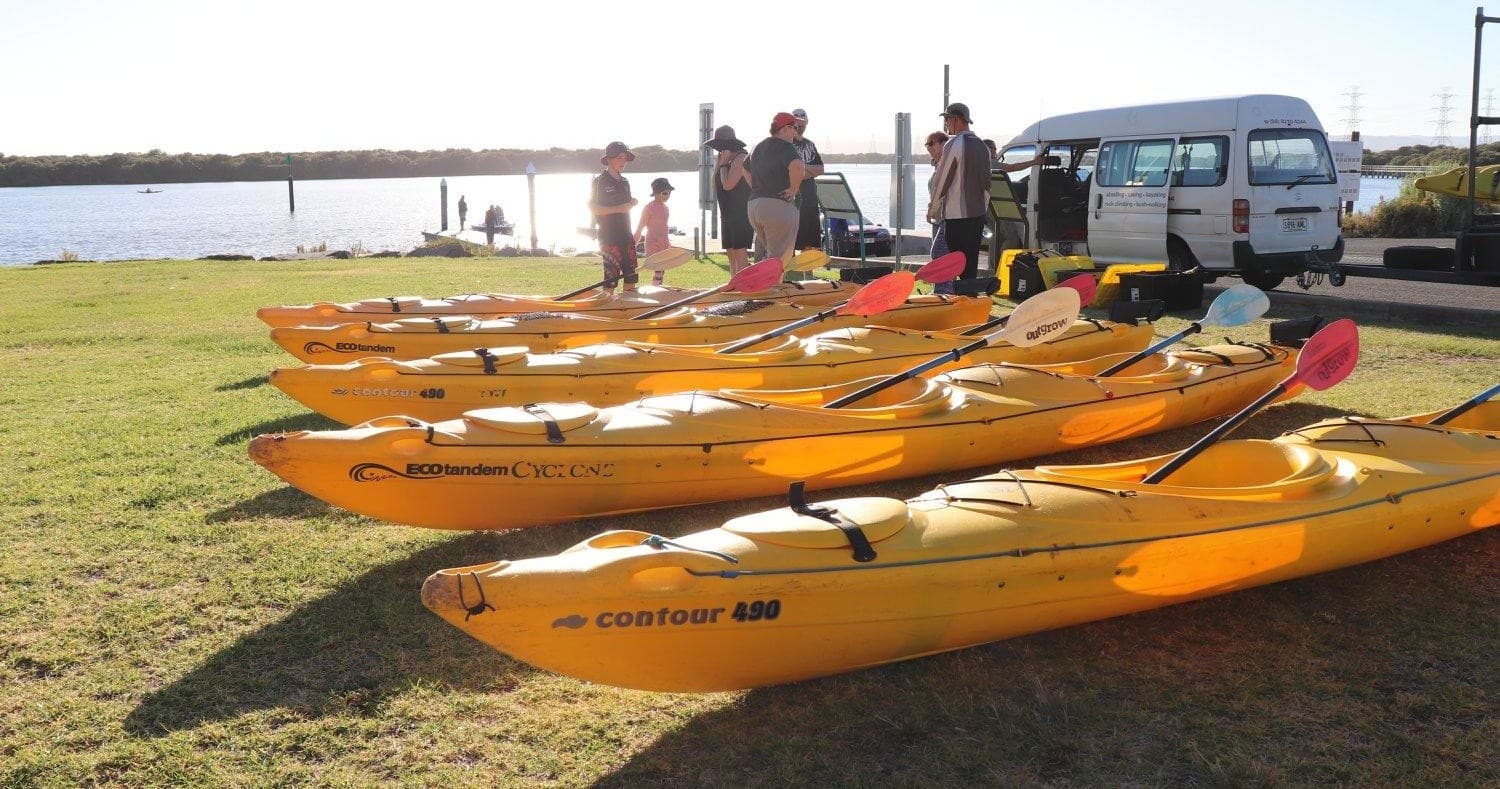 Yellow kayaks lined on waterfront grass ready for coastal tour launch