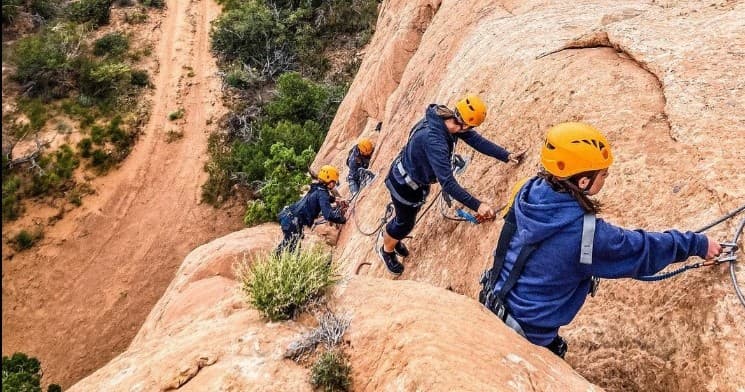 Guided rock climbers ascending sandstone cliff on outdoor via ferrata