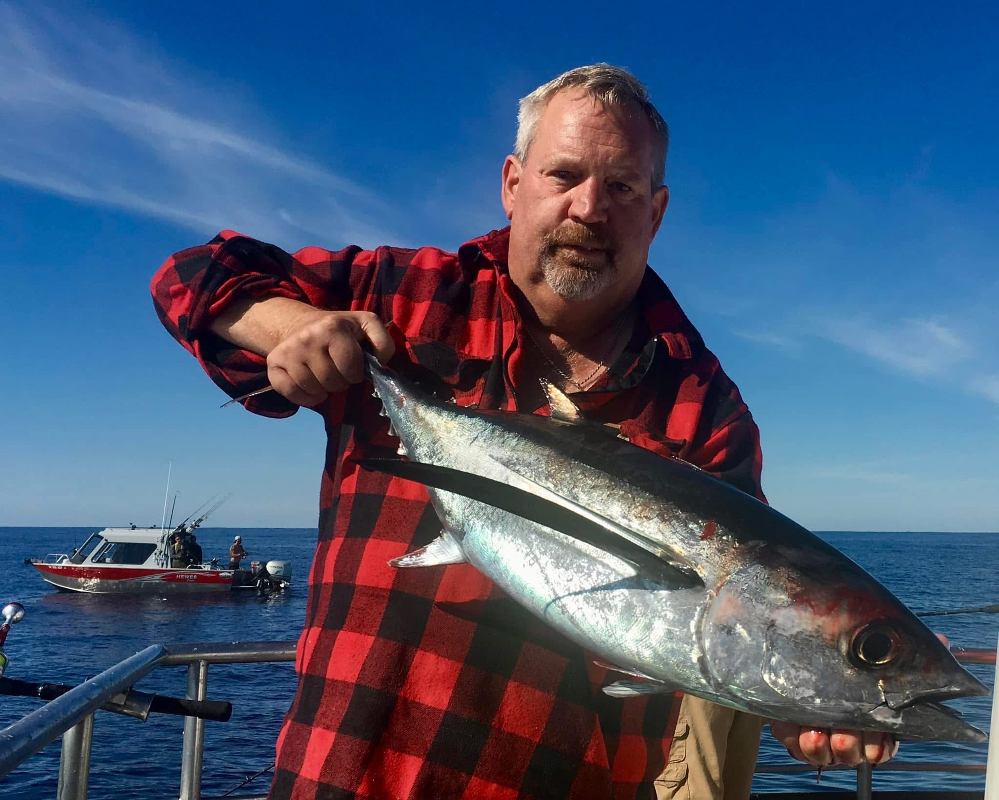 Angler holding tuna with coastal fishing boats under blue sky