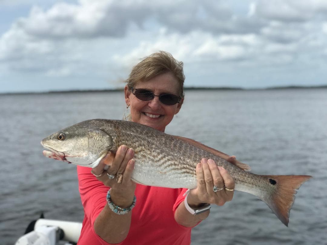 Woman holding redfish on flats with coastal horizon