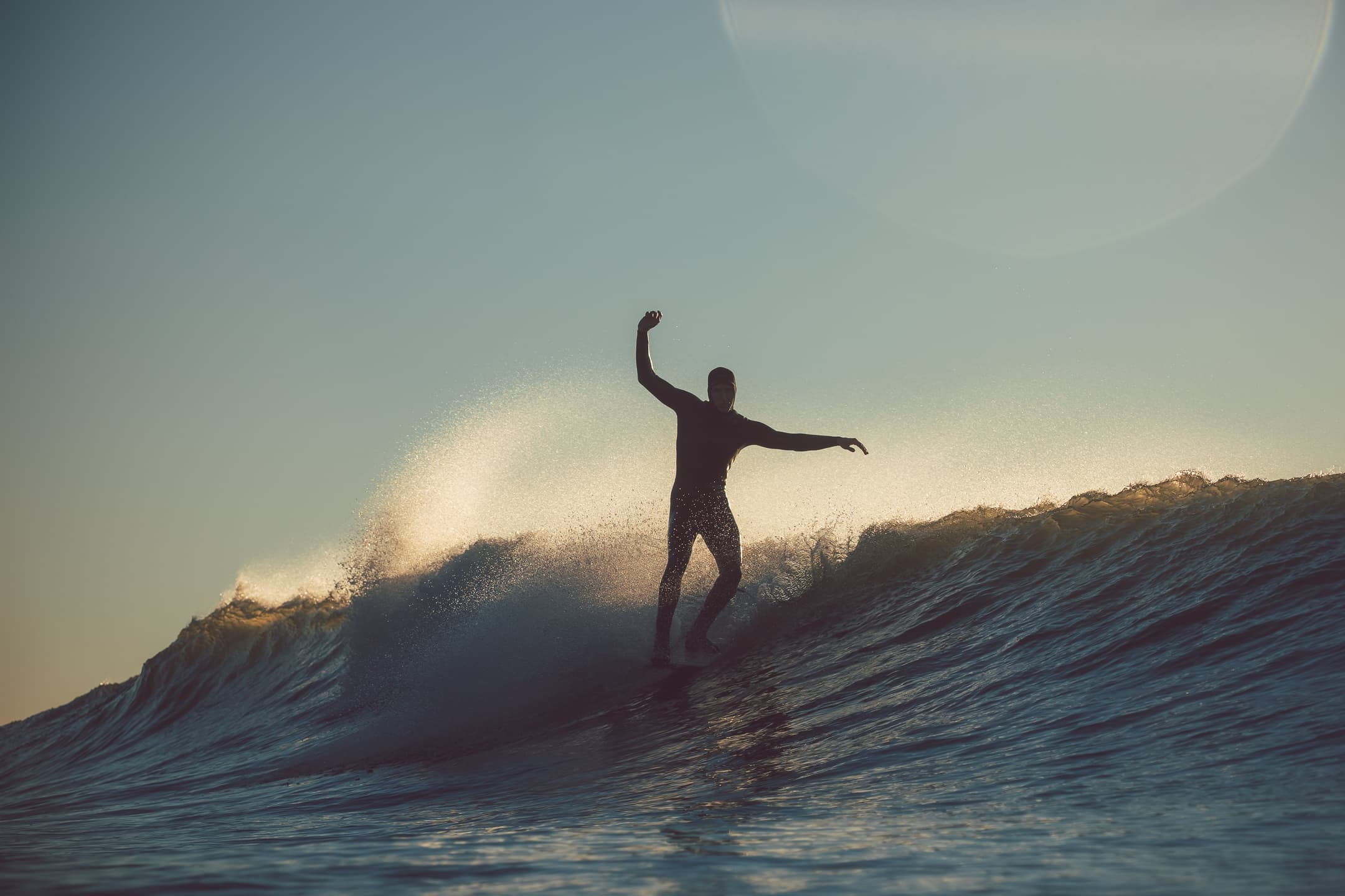 Silhouette surfer riding sunset wave off Croyde Bay shoreline