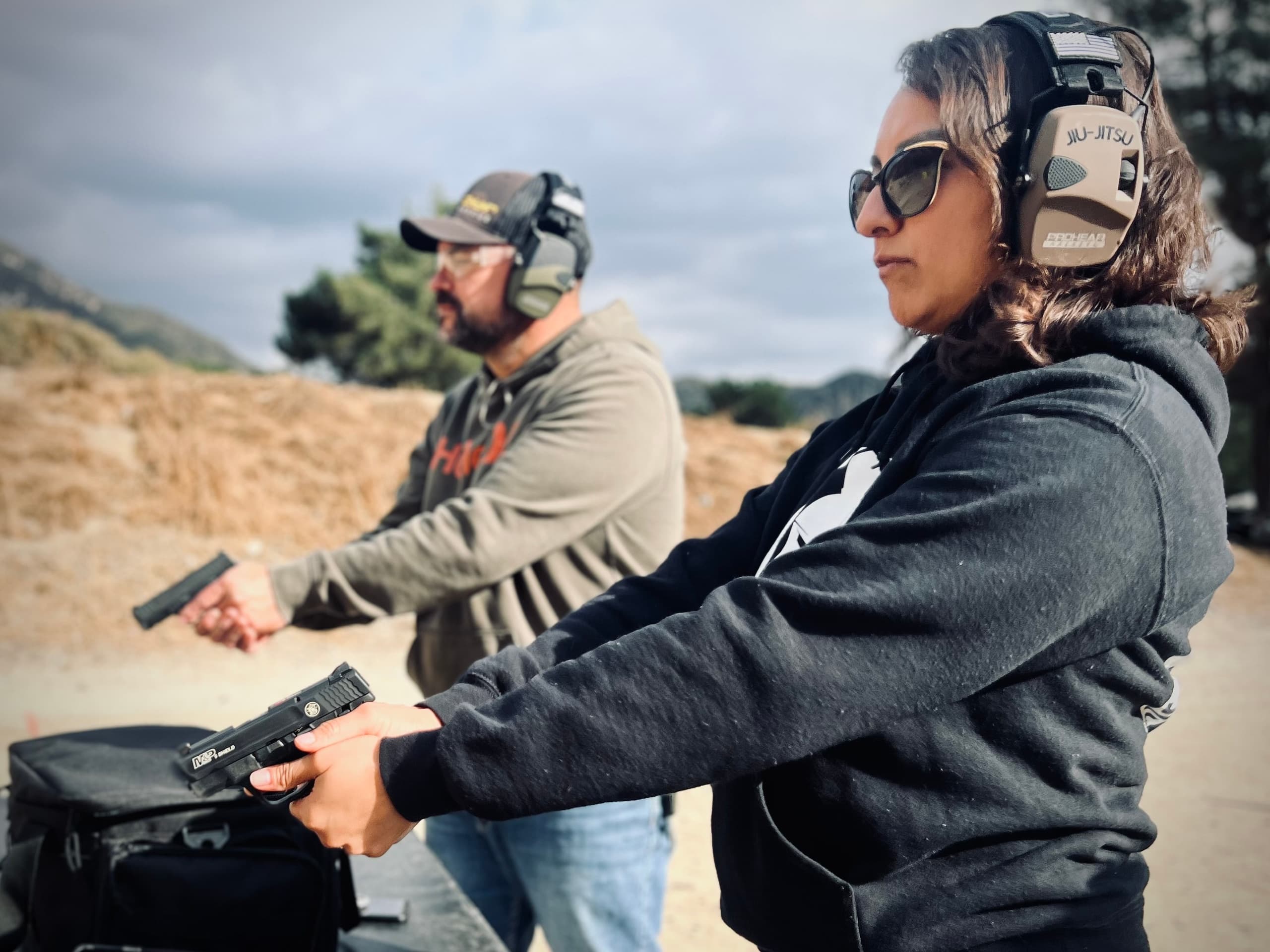Pair of shooters practicing handgun drills at sunny outdoor range