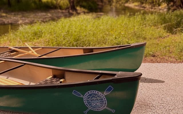 Green canoes beached on sandy riverbank for guided paddling