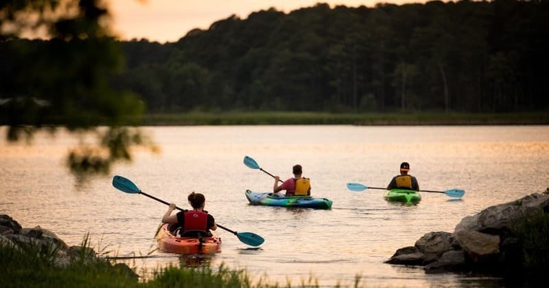 Three kayakers paddling on tranquil sunset lake near shore