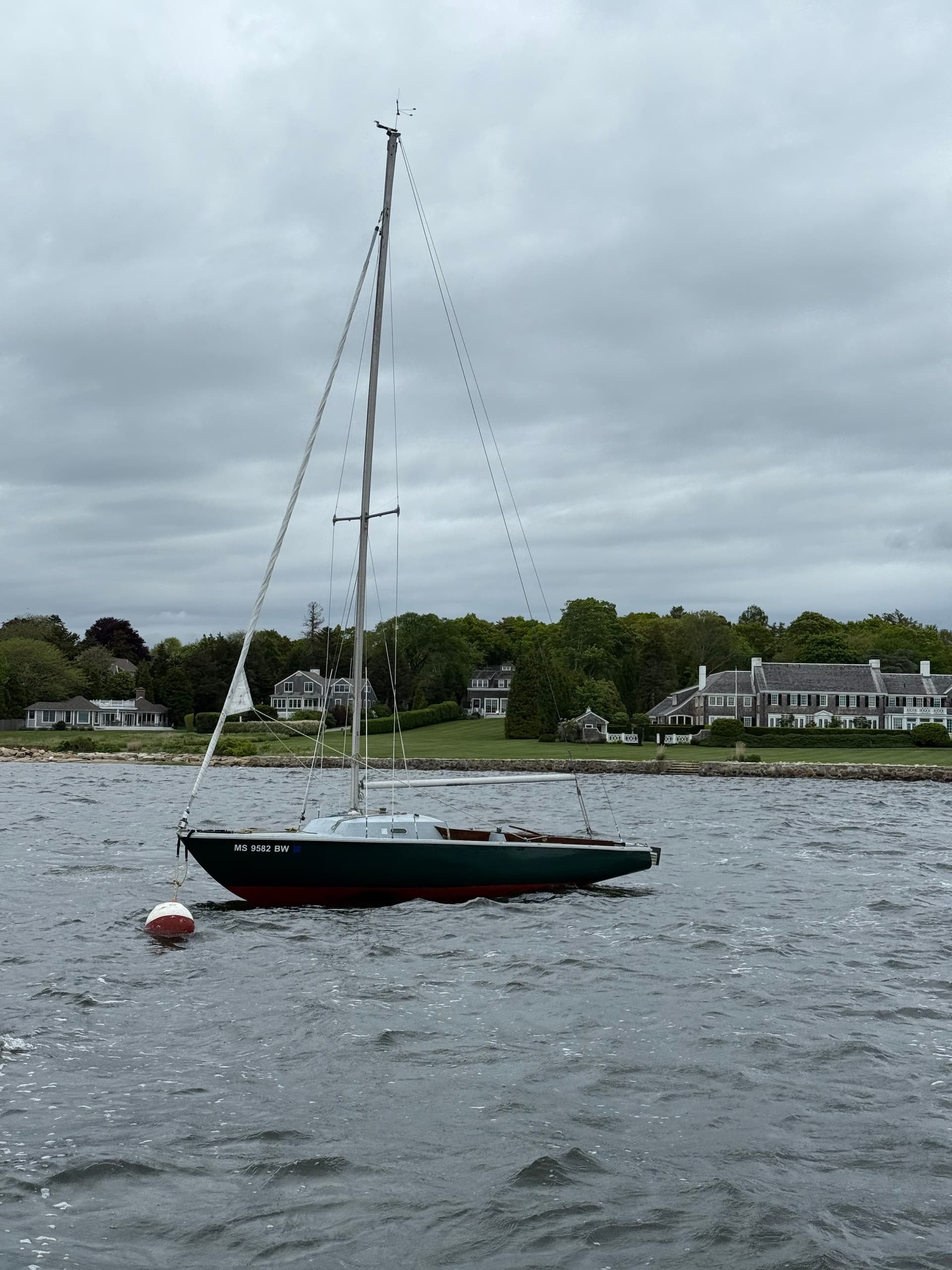 Classic sloop on mooring in choppy coastal bay near shoreline