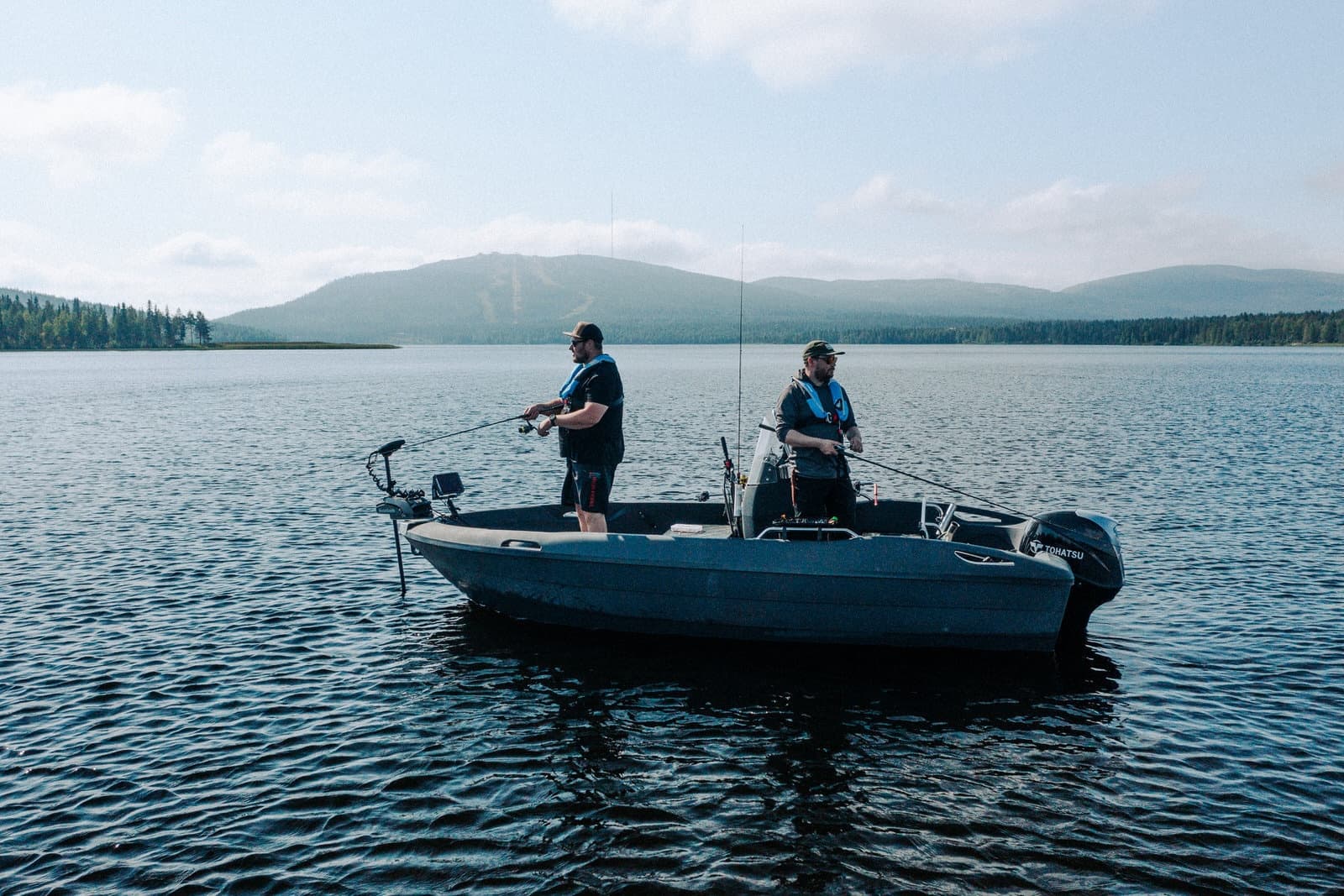 Two anglers standing in fishing boat on wide scenic mountain lake