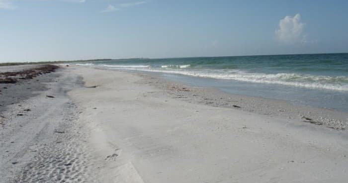 Wide sandy beach shoreline with waves and blue sky