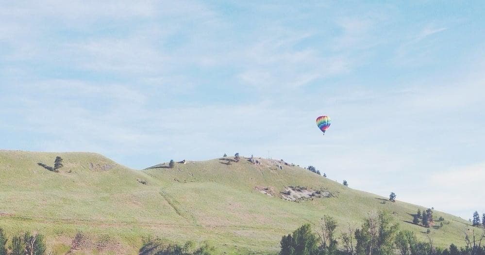 Solo hot air balloon floating over green rolling hills