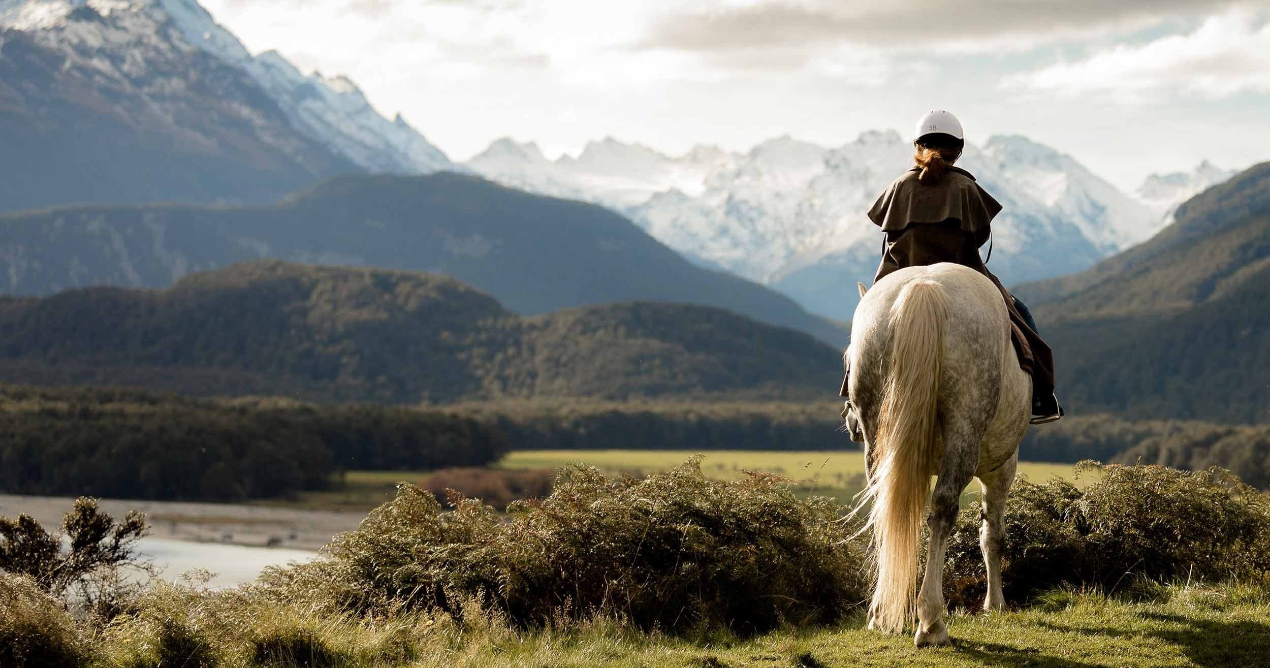 Horseback riding across alpine meadow with mountain vista