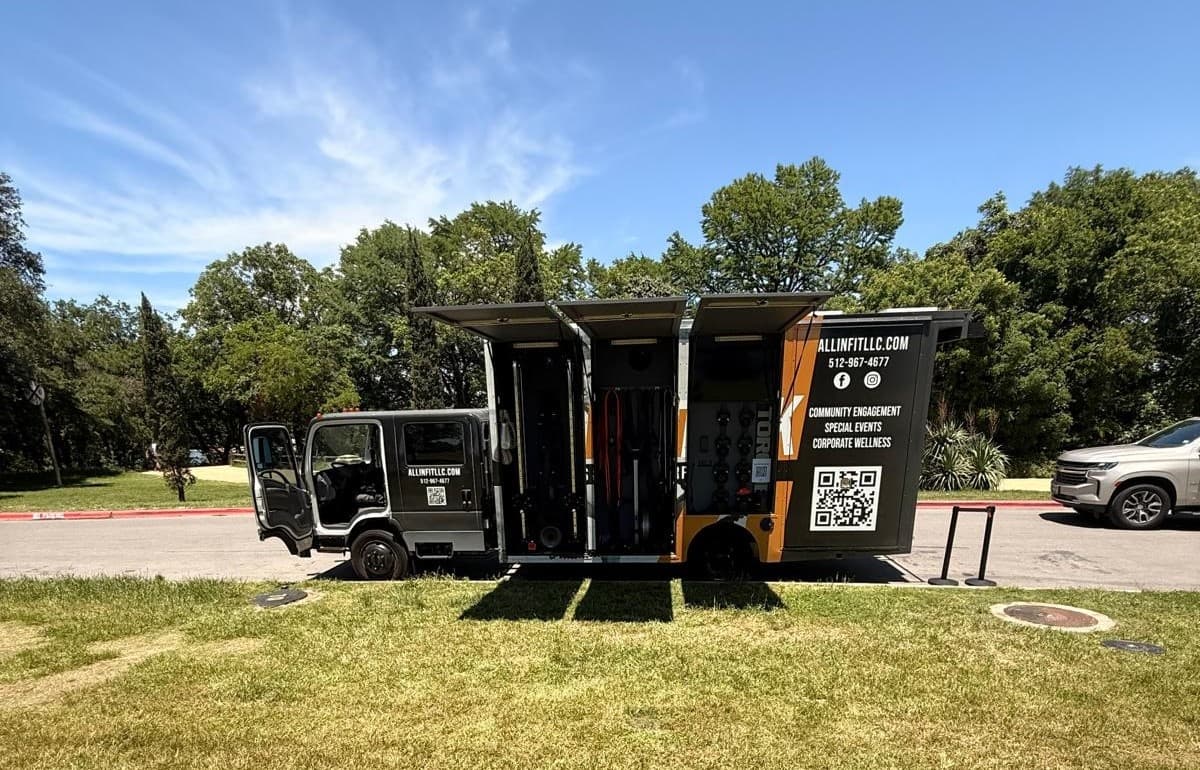 Mobile fitness truck parked on grassy field with trees
