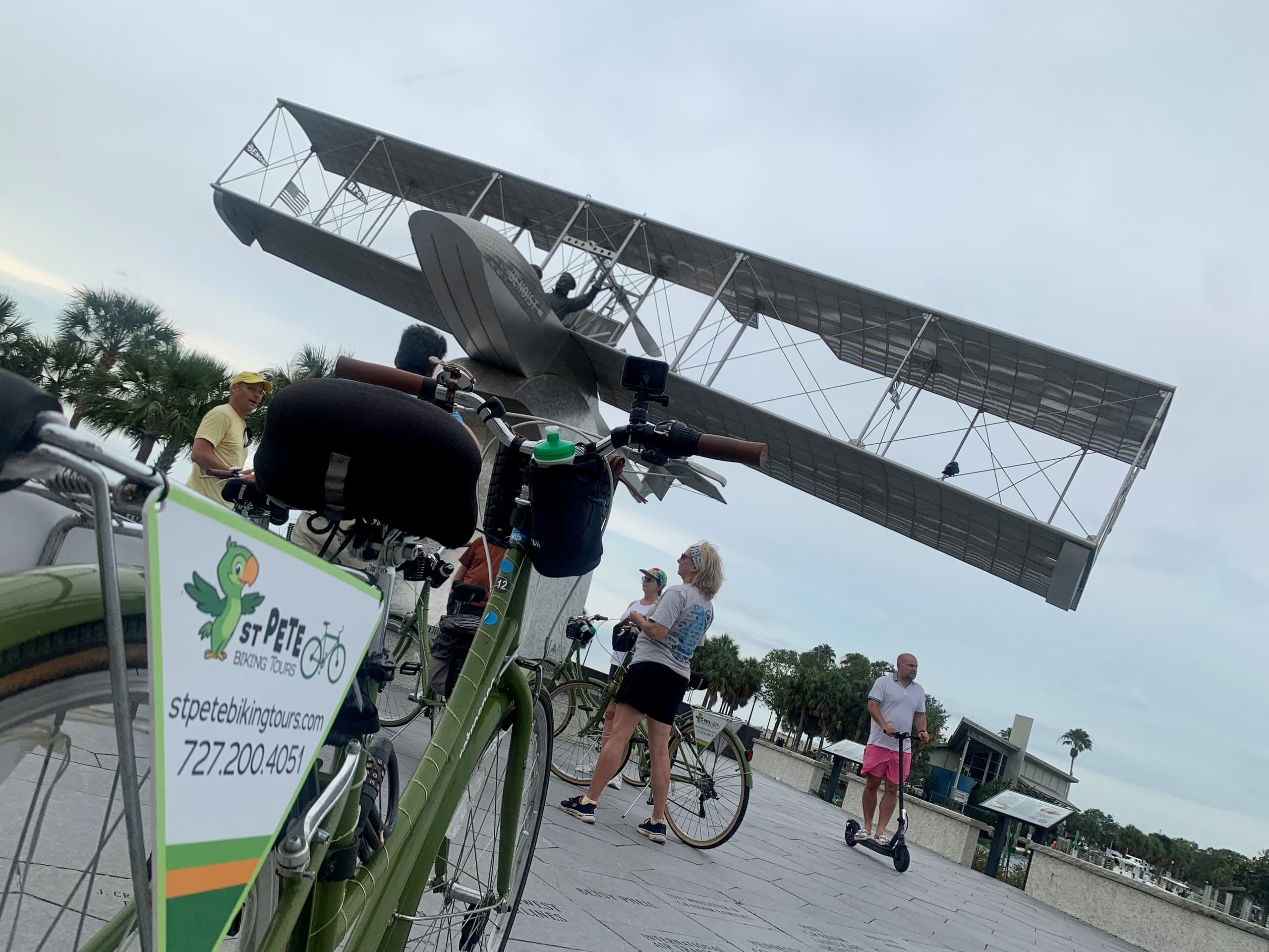 Vintage biplane flyover with parked tour bikes at waterfront plaza