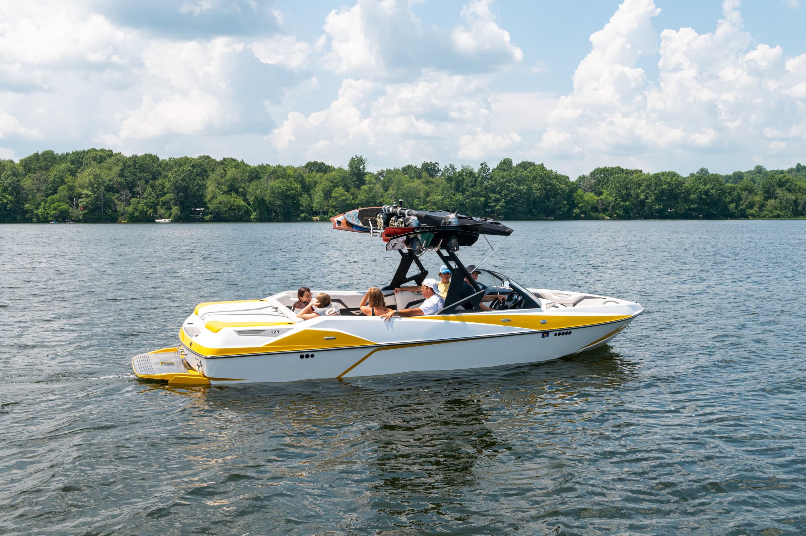 Wakeboard boat anchored on lake with sunny tree-lined shore