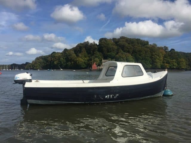 Small hire motorboat moored on estuary with wooded island backdrop