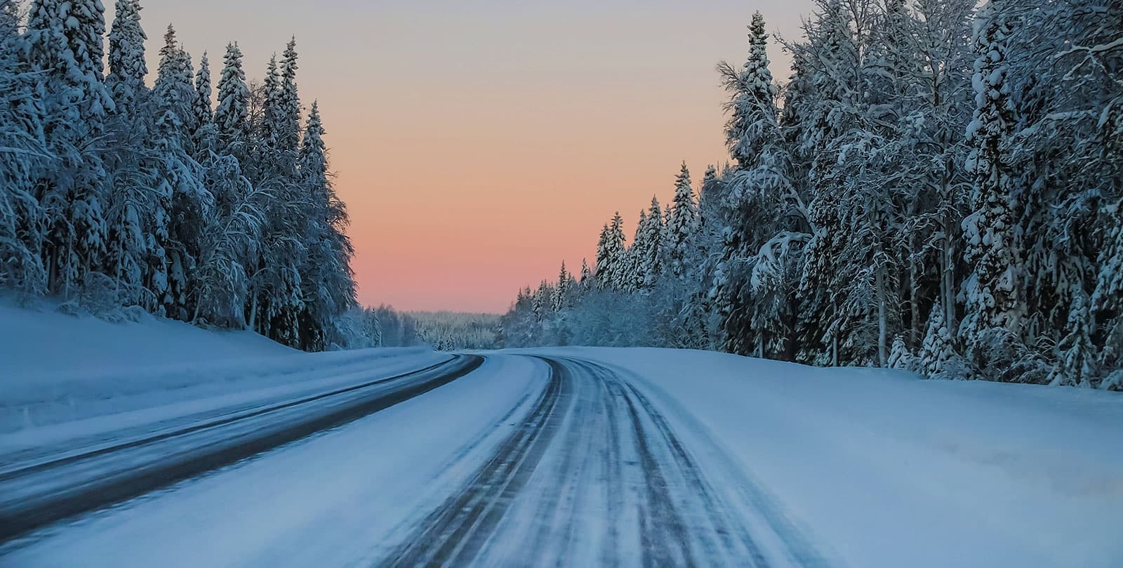 Snow-covered highway through pine forest at winter sunset, Lapland