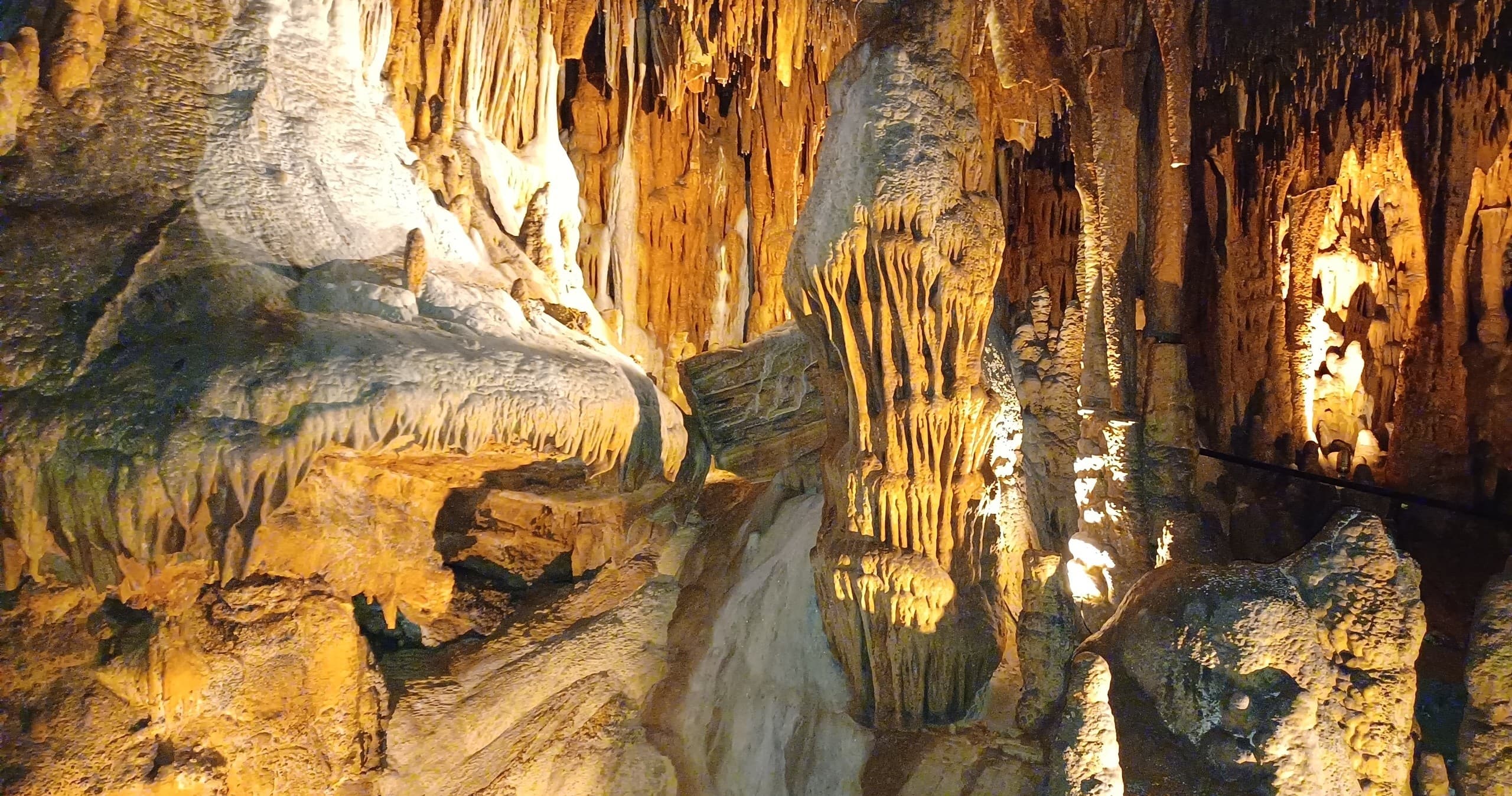 Illuminated cavern chamber with reflective pool, guided cave tour