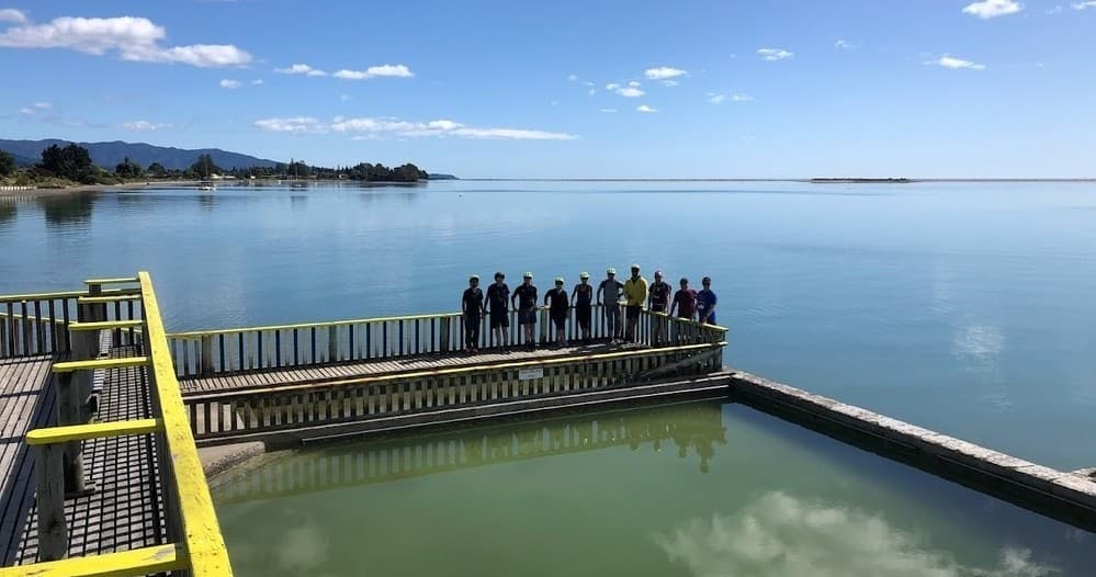 Group standing on pier over calm blue water enjoying coastal vista