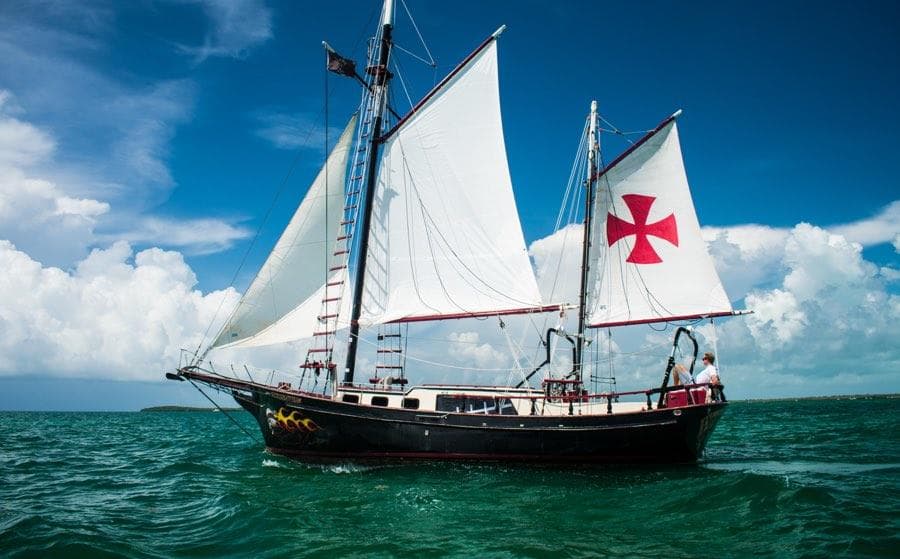 Historic tall ship sailing on turquoise ocean under blue sky