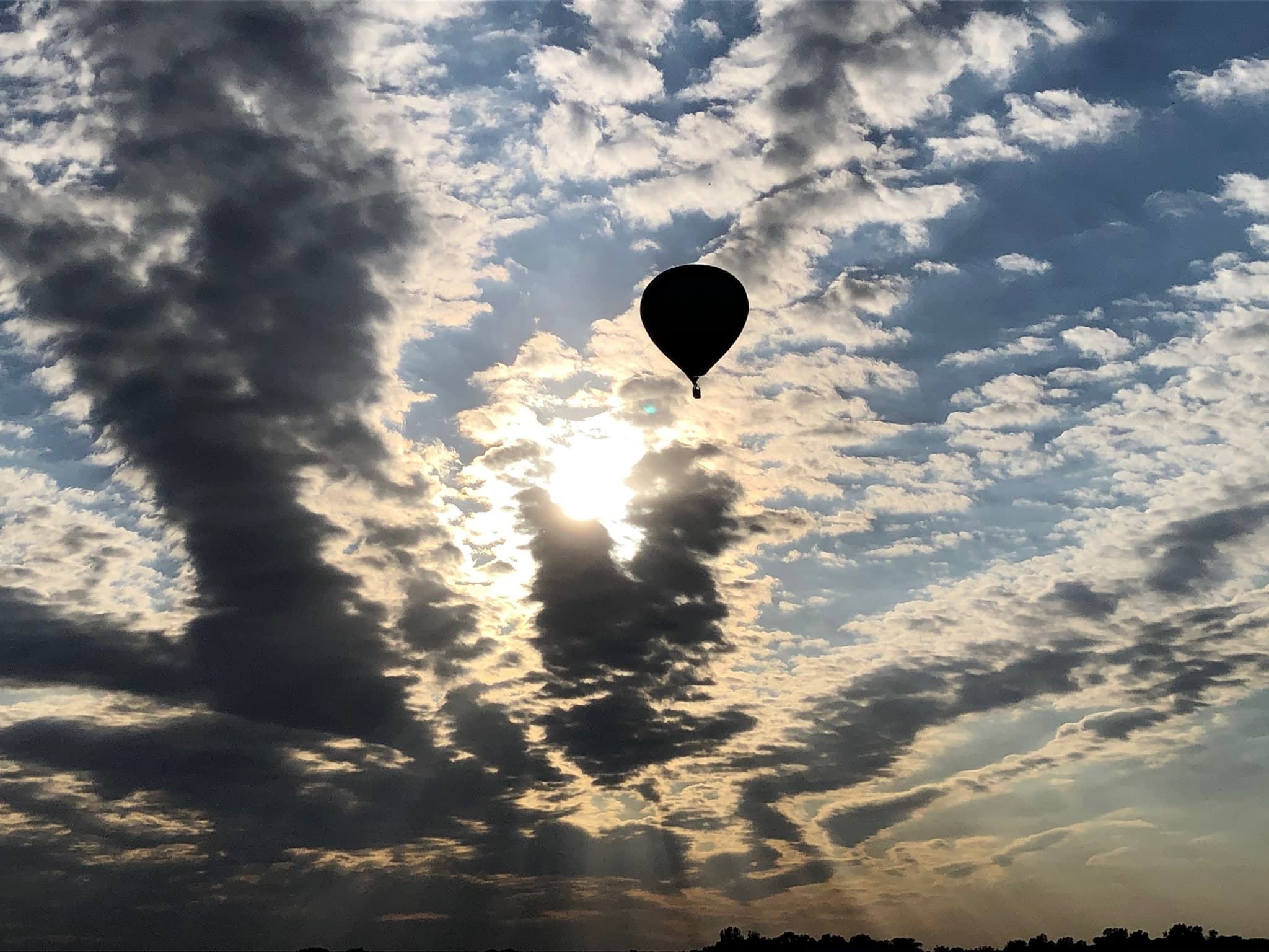 Hot air balloon silhouetted against dramatic cloudy sunrise sky
